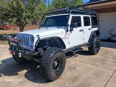White Jeep Wrangler with off-road modifications parked on a driveway.
