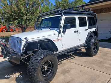 White lifted Jeep Wrangler with off-road tires and roof rack.