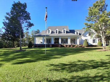 Large white house with a porch and American flag on a sunny day.