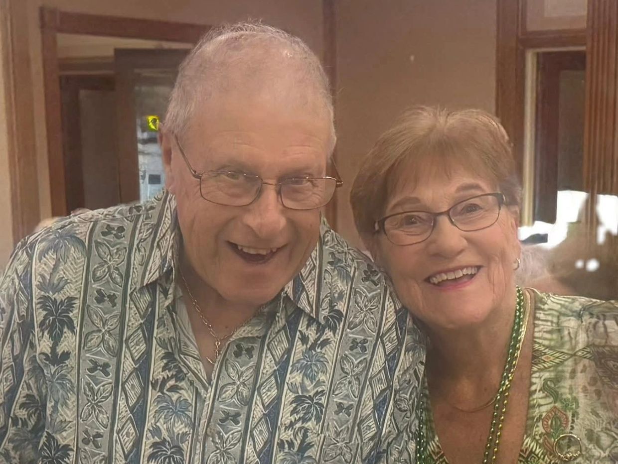 Smiling elderly couple in patterned shirts and glasses.