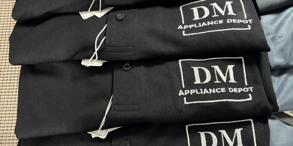 Stack of black shirts with DM Appliance Depot logo.