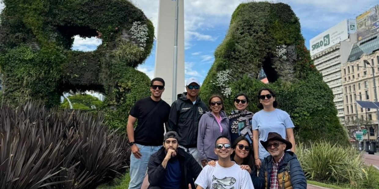 Grupo de personas frente a esculturas verdes con forma de letras.