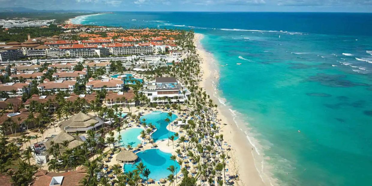 Vista aérea de resort frente a la playa con piscina y mar turquesa.