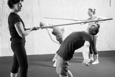 Class performing back bends under a stick, promoting flexibility of the spine
