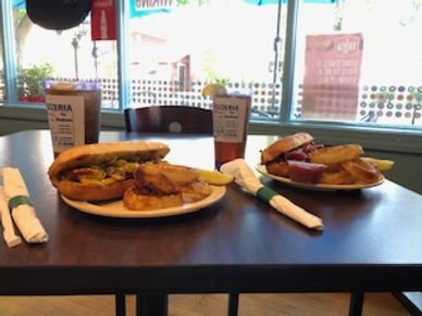 Two plates of sandwiches with fries and drinks on a restaurant table.