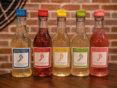 Five bottles of Barefoot wine in different flavors lined up on a wooden table.