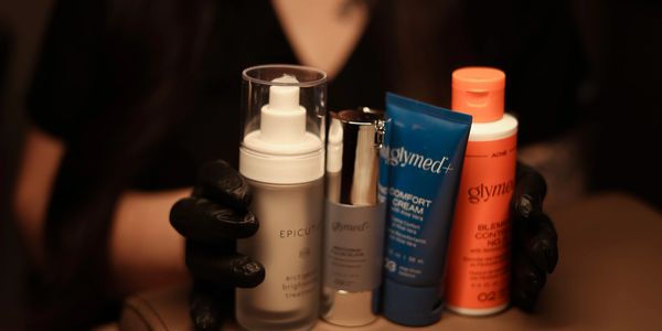 A person in black gloves holds four skincare products in warm lighting.