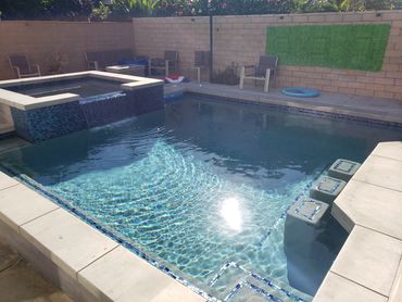 A clean backyard pool with an attached spa and sunlight reflecting on the water.