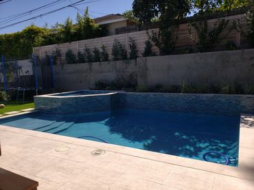A backyard pool with a built-in spa and trampoline in the background.