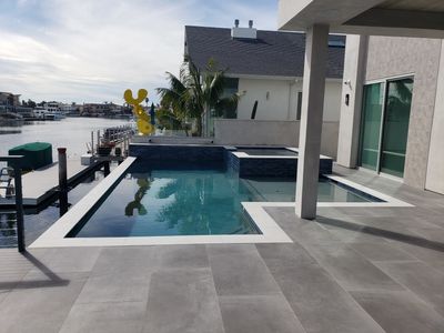 Waterfront pool and spa with a blue interior finish and covered patio
