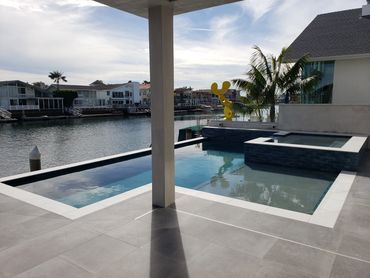 Modern backyard with a pool, hot tub, and waterfront view.