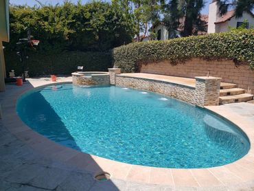 Oval pool with raised spa, stone waterfall wall, and blue waterline tile