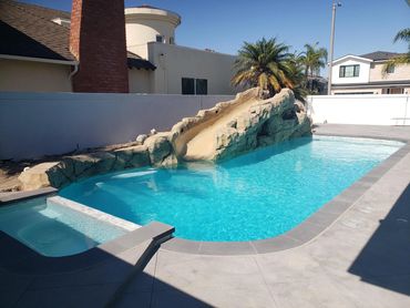 Pool with a rock slide, sun shelf, and gray coping