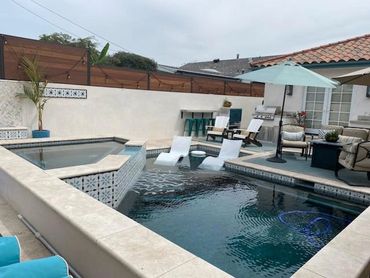 Pool and raised spa with patterned tile accents and lounge chairs on a sun shelf