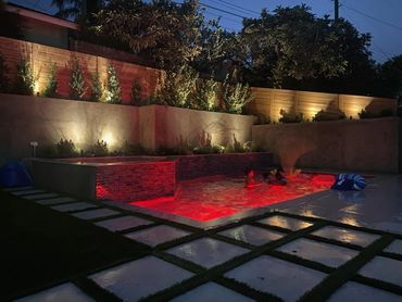 Pool and spa lit red at night with stone wall lighting and stepping-stone pavers