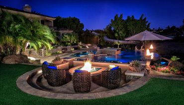Backyard pool at night with fire pit seating, spa, and fire features