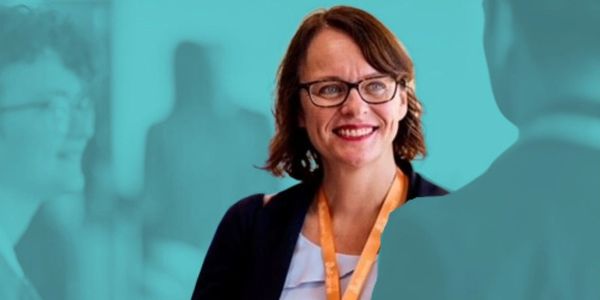 Smiling woman with glasses and orange lanyard in a professional setting.