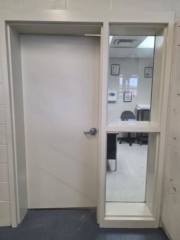 White door with window showing a chair and desk inside.