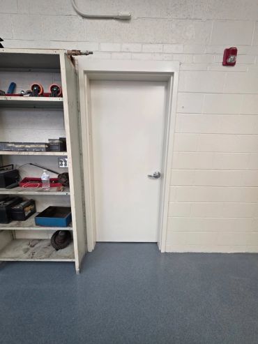 Closed white door next to a metal shelf in a workshop.