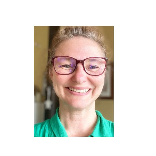 Close up image of a woman's face. She is smiling. She is wearing glasses.