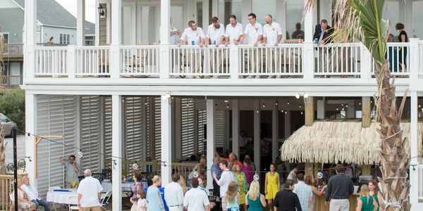 A lively outdoor gathering with guests socializing on a two-story deck under string lights.