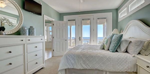 Bright bedroom with white furniture and ocean view through glass doors.