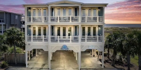 Beachfront house with balconies and palm trees at sunset.
