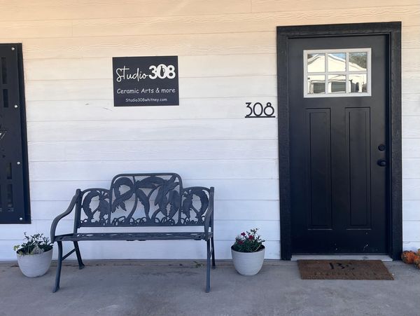 Front door image of Studio 308, Black and white building with a bench to sit on.