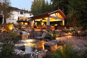 Elegant backyard with waterfall, gazebo, and cozy lighting at dusk.