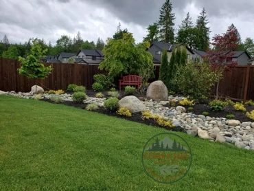 A landscaped backyard with a red bench, rocks, shrubs, and a wooden fence under cloudy skies.