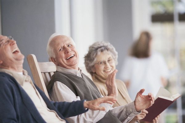 Happy seniors from nursing house spending day outside and reading book together