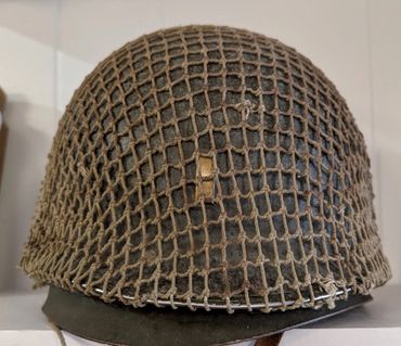 Military helmet with netting and insignia on display.
