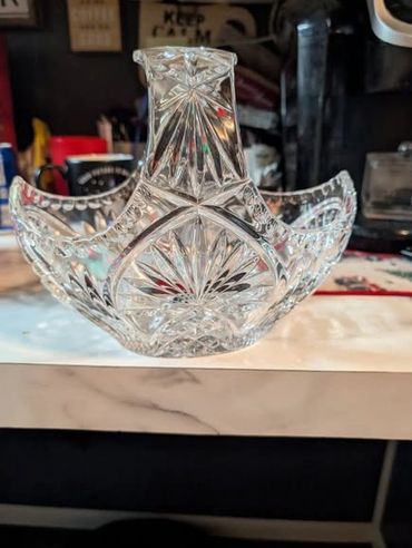 Intricately designed clear glass basket with a handle on a marble surface.