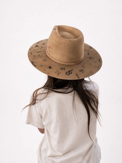 Woman wearing a custom tan cowboy hat with a hand-burned brand pattern across the brim