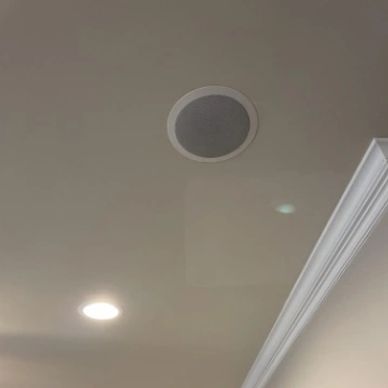 Ceiling speaker and recessed light in a room with crown molding.