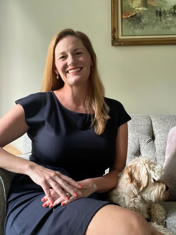 Smiling woman in black dress sitting on a sofa with a small dog.
