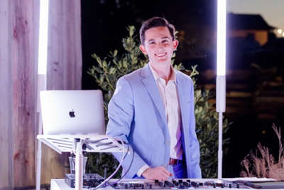 A smiling DJ in a light blue suit performing outdoors at night.