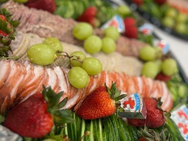 A fresh platter with sliced meats, strawberries, grapes, cucumbers, and cheese wedges.