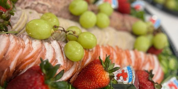 A fresh platter with sliced meats, strawberries, grapes, cucumbers, and cheese wedges.