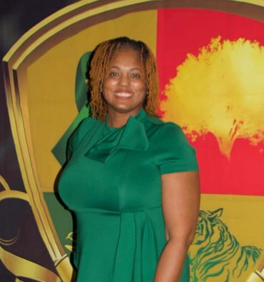 A smiling woman in a green dress stands before a colorful backdrop.