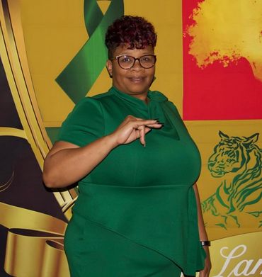 Woman in green dress posing with a hand gesture in front of a colorful backdrop.