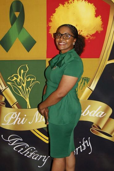 Woman in a green dress posing in front of a Phi Mu Alpha banner.