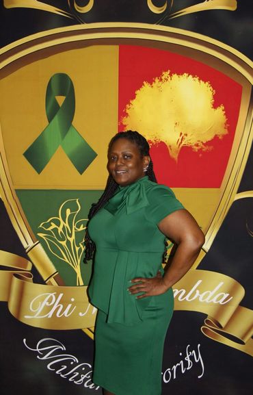 A woman in a green dress poses confidently in front of a colorful emblem.