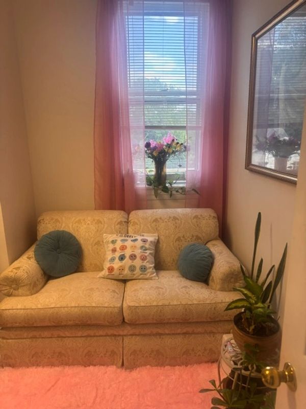 Cozy beige couch with decorative pillows and flowers by window.