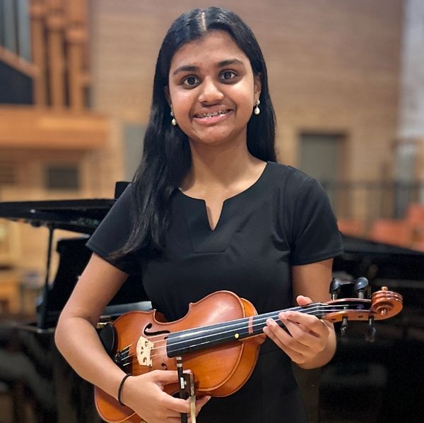 Young woman smiling, holding a violin in a music hall.