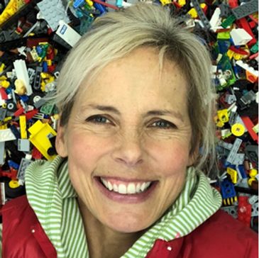 Smiling woman surrounded by colorful LEGO pieces.