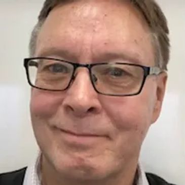 Middle-aged man with glasses smiling in a casual setting.