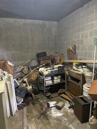 Cluttered storage room with desks, electronics, and industrial debris before cleanout