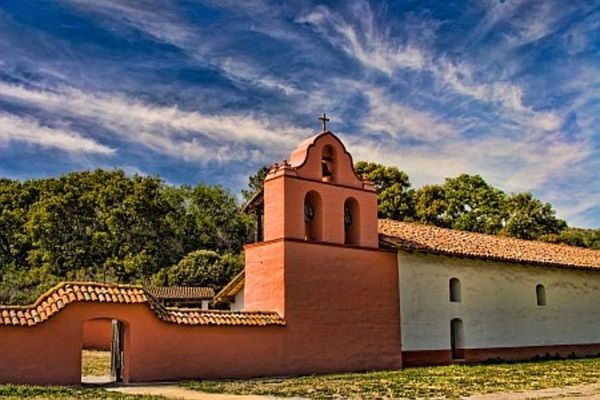 Old mission church with red walls and bell tower.