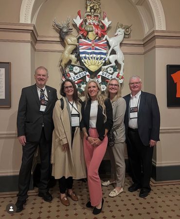 Five professionals posing in front of a large ornate crest inside a formal building.